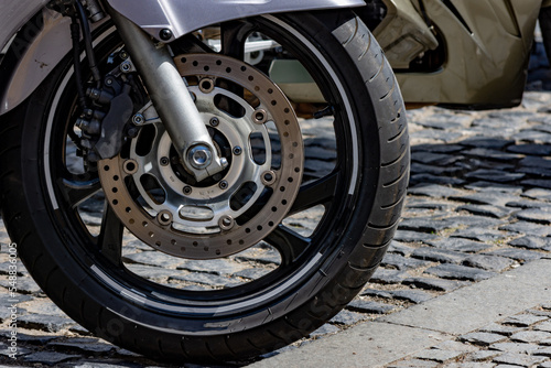 Close up to a sport motorcycle front wheel with breaking disk parked on asphalt