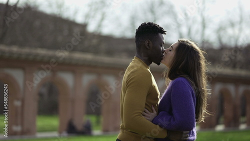 Black man kissing white girlfriend standing outside at park