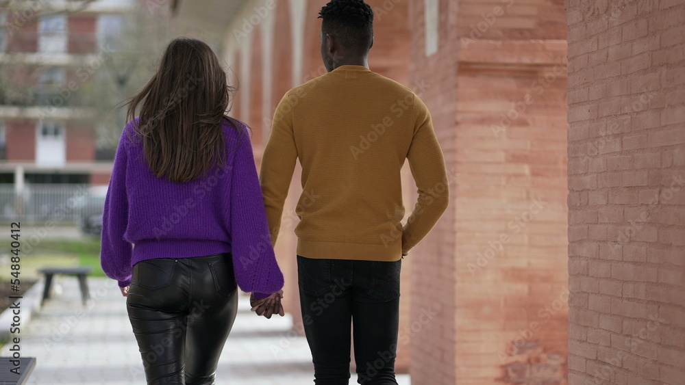 Back of couple walking outdoors holding hands