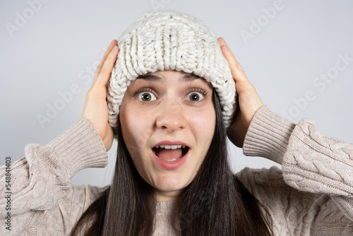 A young brunette woman in a hat and sweater looks into the camera and screams holding her hands to her head.