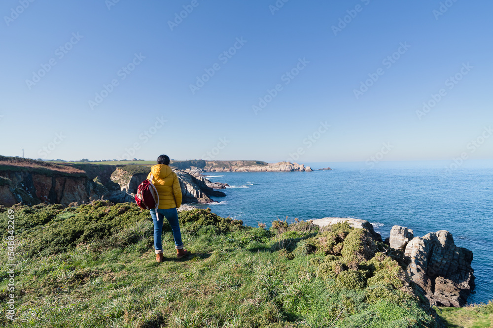 Coastal landscape and girl in yellow hooded coat looking at sea and walking. Copy space.