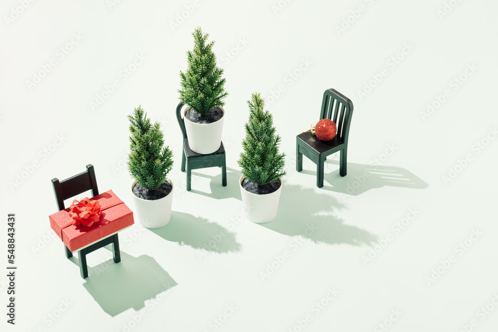 Christmas trees, red gift box and Christmas bauble on black chairs against bright green background. Minimal New Year concept. Winter holidays creative composition. Festive season aesthetic. Christmas trees, red gift box and Christmas bauble on black chairs against bright green background. Minimal New Year concept. Winter holidays creative composition. Festive season aesthetic.