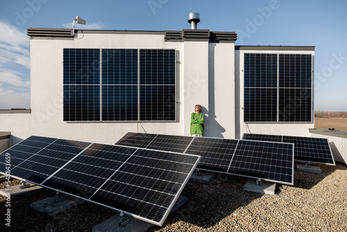 Wide view from above on a solar power plant installed on rooftop of household on nature, happy owner stands on it. Alternative energy, independence and sustainable lifestyle concept