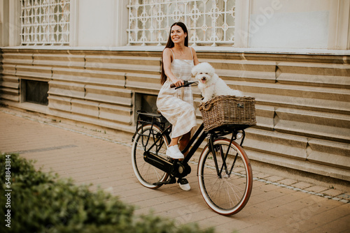 Tableau sur toile Young woman with white bichon frise dog in the basket of electric bike