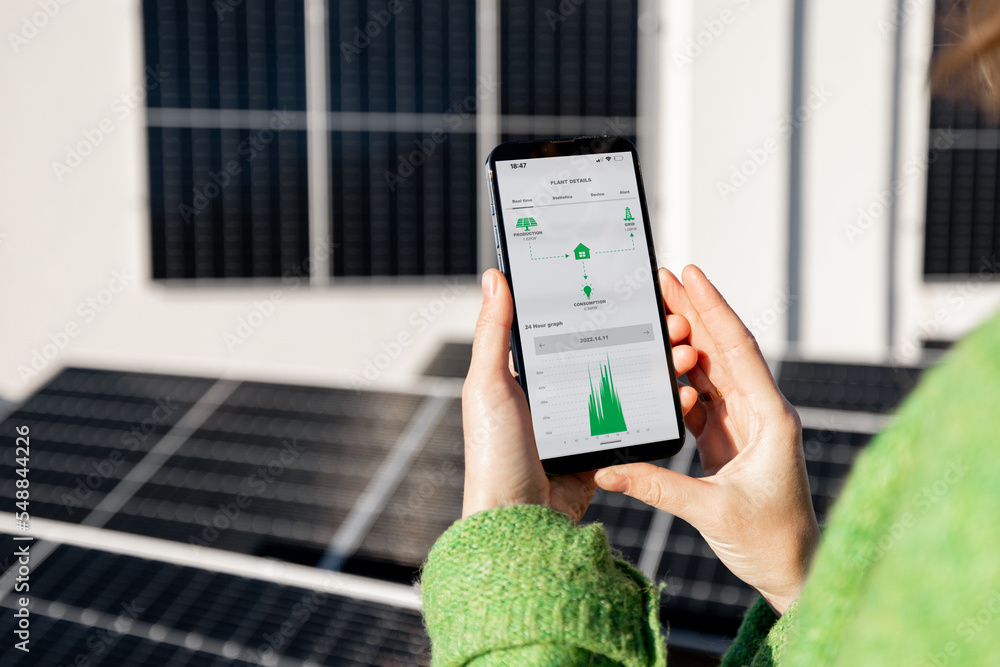 Woman monitors energy production from the solar power plant with mobile phone. Close-up view on phone screen with running program. Concept of remote control of solar energy production - obrazy, fototapety, plakaty 