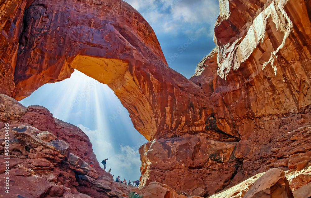 Beautiful spectacular red sandstone arch window cliff landmark, unrecognizable people group, blue summer sky sun rays- Double Arch, Arches National Park, Utah