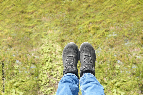 Legs in black sneakers against the background of green grass. Rise in an open chairlift. © Lexis_Jan