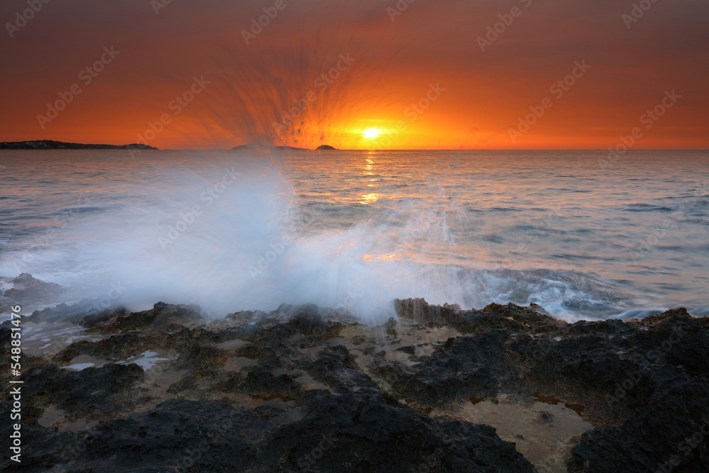 Sunrise image of waves splashing on the rocks at Bombay beach, Santa Eulalia, Ibiza, Spain.