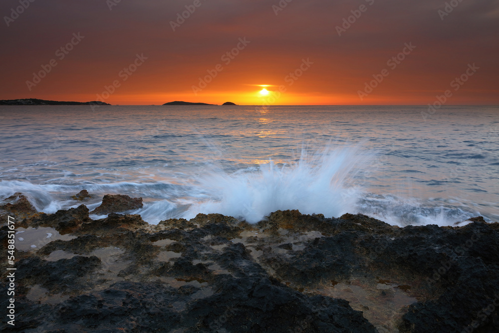 Sunrise image of waves splashing on the rocks at Bombay beach, Santa Eulalia, Ibiza, Spain.