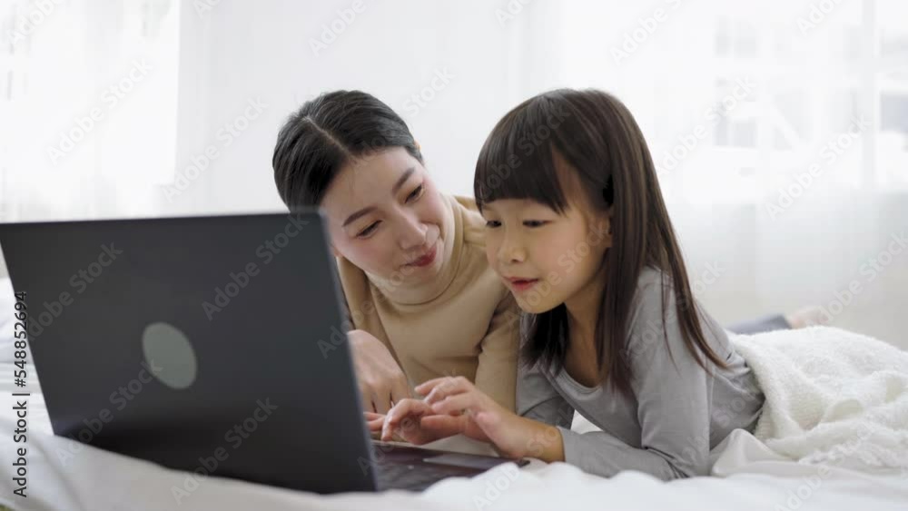 Young happy woman with cute little daughter looking at laptop computer playing on the bed, enjoying technology network together at home bedroom, happy family mothers day, education technology concept Young happy woman with cute little daughter looking at laptop computer playing on the bed, enjoying technology network together at home bedroom, happy family mothers day, education technology concept