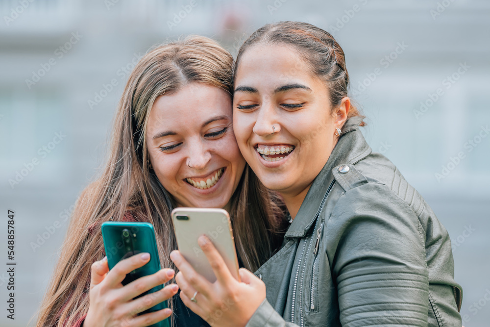 Fototapeta premium friends with mobile phones smiling hugging in the street