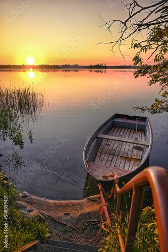 Fotografiet Vertical of a scenic sunset view at the lake with a wooden boat anchored by the
