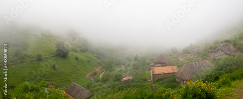 Vistas panorámicas de un pueblo típico rural en la Braña de Pornacal, de Asturias, con techo de paja en verano, un día de niebla blanca y césped verde, España, 2021 photo