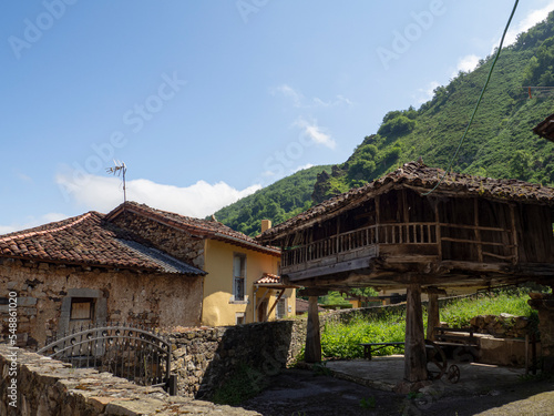 Vistas de un hórreo típico en Villar de Vildas, pueblo de Asturias, en España ,rodeado de casas  y altas montañas verdes detrás, al fondo, verano de 2021. photo