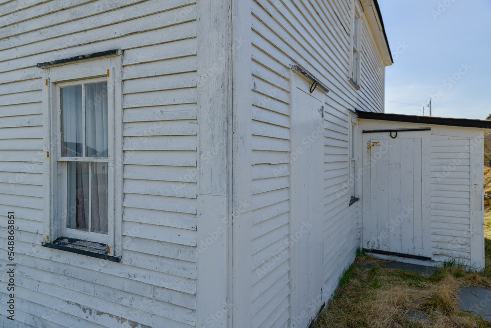 The exterior corner of an old white wooden historic house. There's a porch on the left side of the home along with a window and a couple of wooden doors. Over the doors, there are rusty horseshoes. The exterior corner of an old white wooden historic house. There's a porch on the left side of the home along with a window and a couple of wooden doors. Over the doors, there are rusty horseshoes.