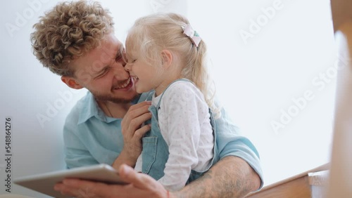 Happy father and daughter rubbing noses and looking at tablet at home photo