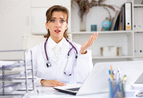 Woman physician sitting at table in her office, looking at camera and speaking.