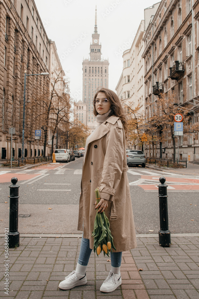 Concept of Poland lifestyle and travel towns in Warsaw. Young beautiful woman walking with bouguet of tulips on Warsaw city. Woman have a beautiful bouquet of yellow tulips standing outdoors in city.