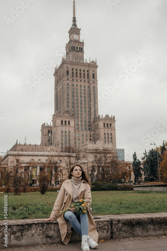 A walk near the Palace of Culture. A girl with yellow tulips against the background of the Palace of Culture in Poland. A pretty girl in glasses with flowers walks in Europe city.