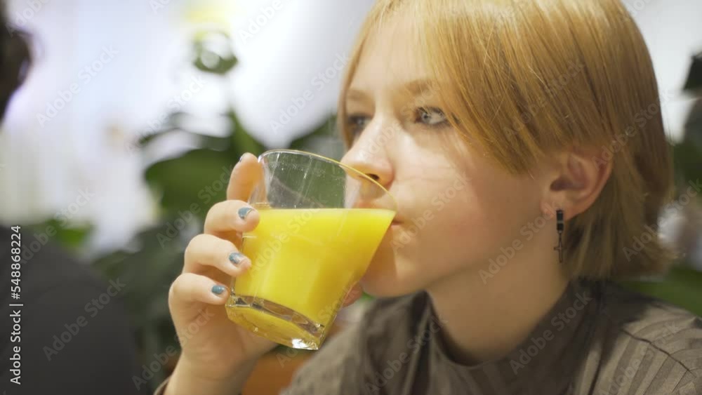 A teenage girl drinks orange juice, looks into a smartphone. Close-up A teenage girl drinks orange juice, looks into a smartphone. Close-up