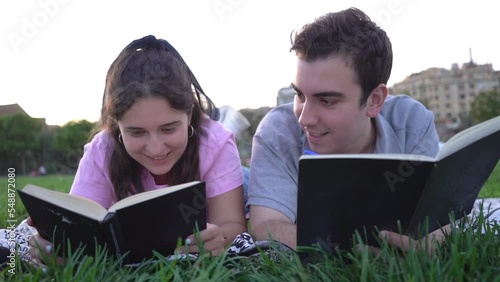 young caucasian woman and man student friends relaxing, having fun, reading and studying in the park