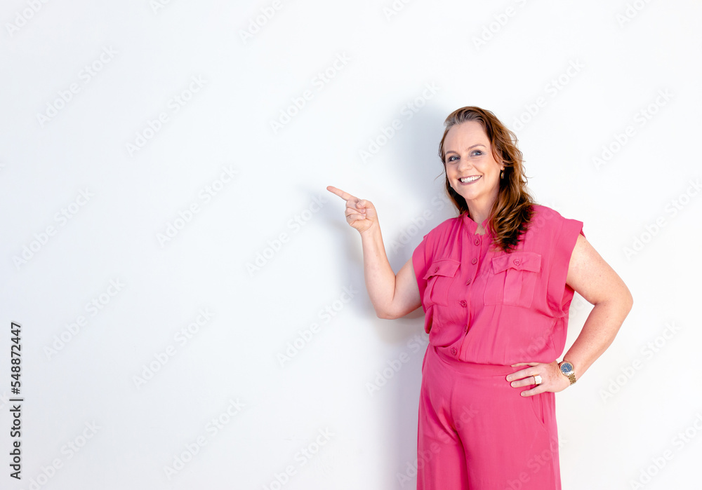Happy mature woman pointing finger to show something with white wall in background Happy mature woman pointing finger to show something with white wall in background