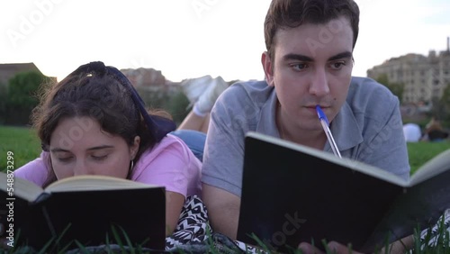 young caucasian woman and man student friends relaxing, having fun, reading and studying in the park