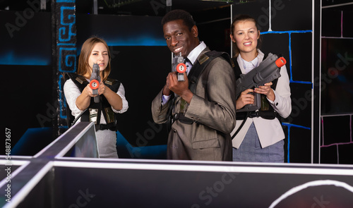 African man and two glad European female in business suits at laser tag room