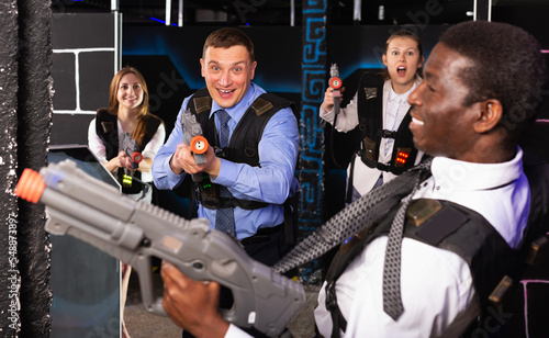 Emotional portrait of active young men and women co-workers having corporate entertainment in laser tag room