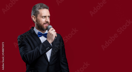 photo of man presenter in tuxedo hold microphone, copy space. tuxedo man presenter isolated on red