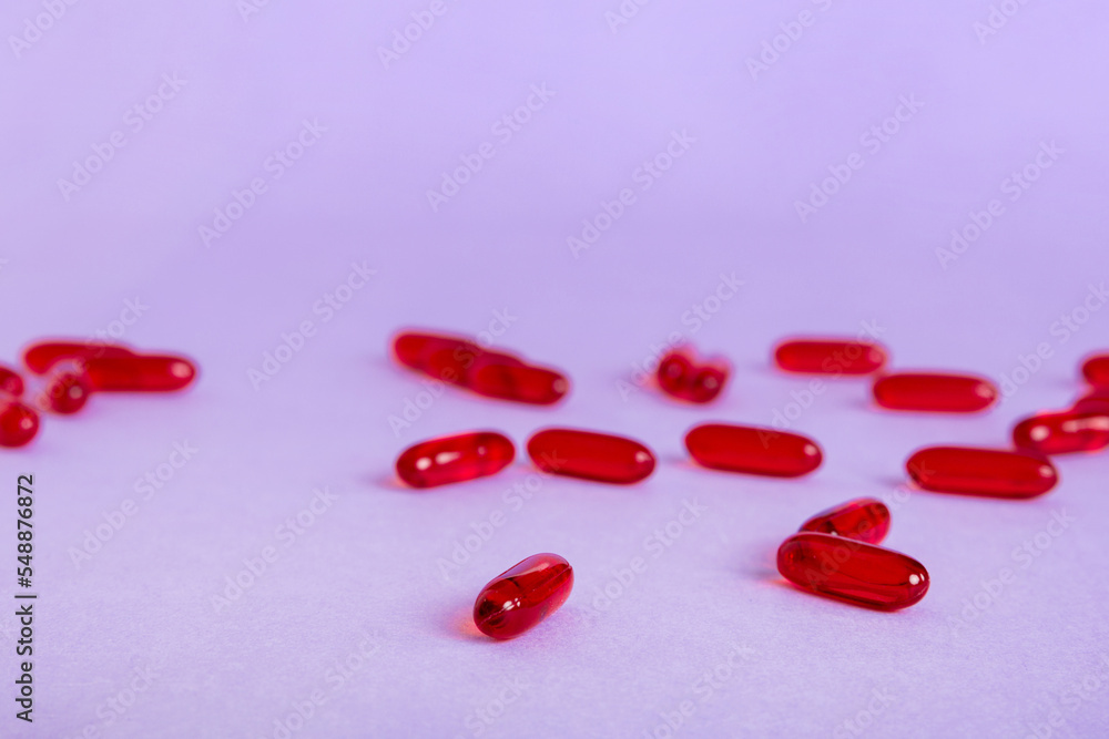 Heap of red pills on colored background. Tablets scattered on a table. Pile of red soft gelatin capsule. Vitamins and dietary supplements concept Heap of red pills on colored background. Tablets scattered on a table. Pile of red soft gelatin capsule. Vitamins and dietary supplements concept