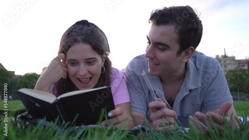 young caucasian woman and man student friends relaxing, having fun, reading and studying in the park