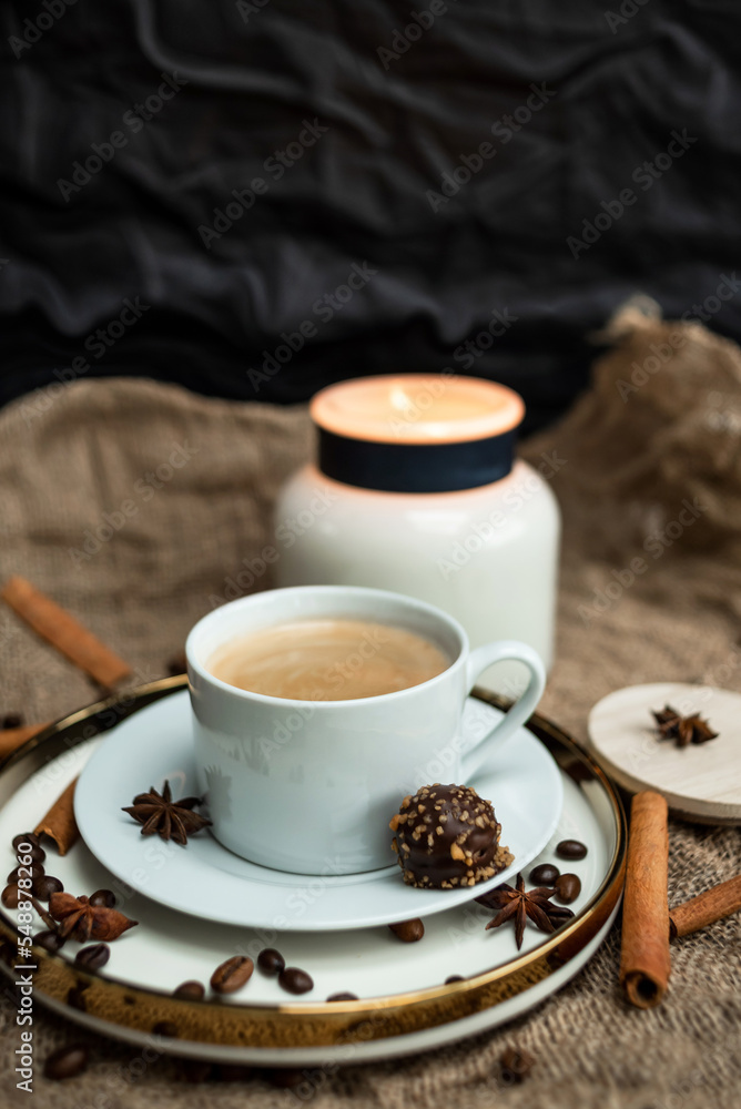 An aesthetic composition of a cup of black coffee with foam and a burning candle, decorated with chocolates, anise stars, coffee beans and cinnamon sticks An aesthetic composition of a cup of black coffee with foam and a burning candle, decorated with chocolates, anise stars, coffee beans and cinnamon sticks