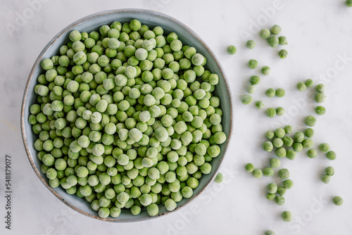 Overhead view of a bowl of frozen green peas on a table photo