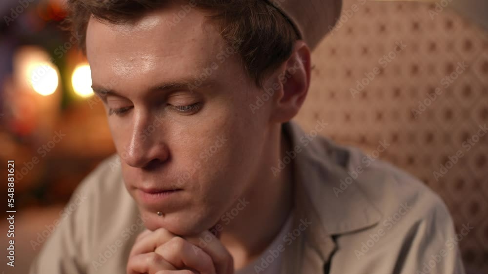 Close-up face of thoughtful young man sitting indoors on New Year's eve and looking away smiling. Happy excited Caucasian LGBT guy rejoicing guests at home on Christmas. Headshot portrait Close-up face of thoughtful young man sitting indoors on New Year's eve and looking away smiling. Happy excited Caucasian LGBT guy rejoicing guests at home on Christmas. Headshot portrait