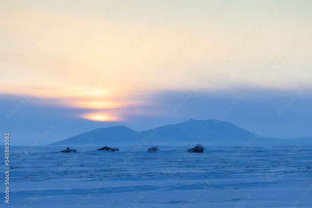 Winter arctic landscape. View of the snow-covered tundra and snow-capped mountains. Abandoned houses in the tundra in the Arctic. Cold winter weather. Sunset. Northern nature. Harsh polar climate. Winter arctic landscape. View of the snow-covered tundra and snow-capped mountains. Abandoned houses in the tundra in the Arctic. Cold winter weather. Sunset. Northern nature. Harsh polar climate.