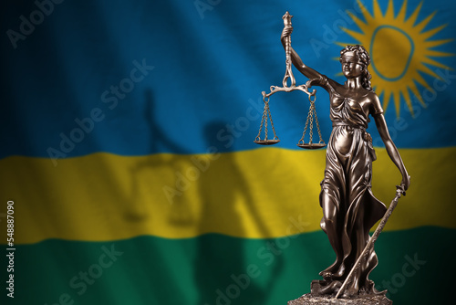 Rwanda flag with statue of lady justice and judicial scales in dark room. Concept of judgement and punishment photo