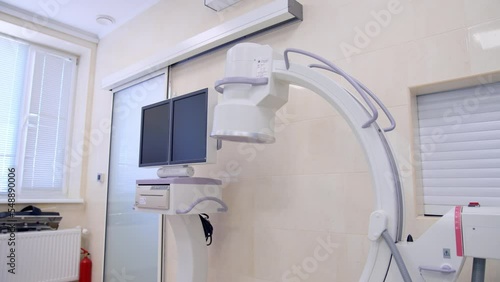 C-Arm fluoroscopy machine standing in the modern surgery room. Operational table with lung ventilation system standing nearby. photo