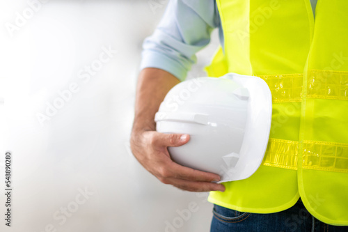 Engineer holding hardhat wearing yellow vest and standing ready for work safety in site.