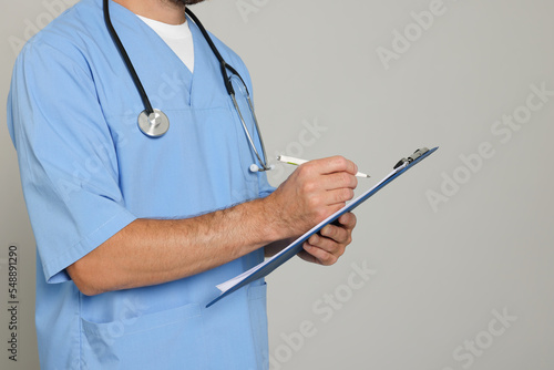 Doctor with stethoscope and clipboard on light grey background, closeup