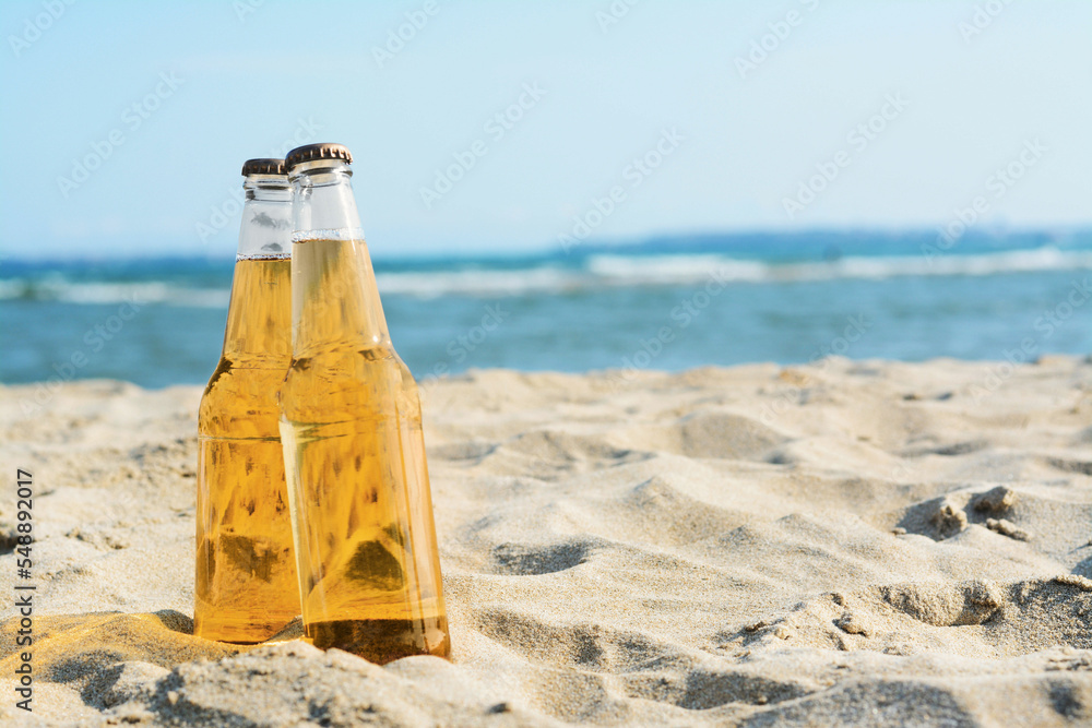 Bottles of cold beer on sandy beach near sea, space for text - obrazy, fototapety, plakaty 
