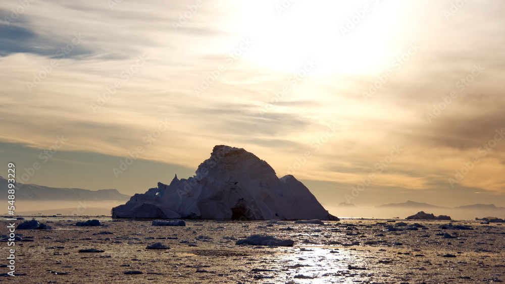 Sun silhouetting a large iceberg floating in the Southern Ocean, at Cierva Cove, Antarctica, at sunset