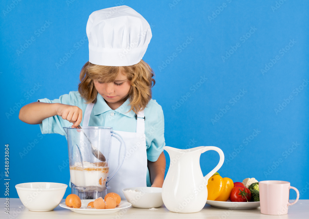 Kid boy in chef hat and apron cooking preparing meal. Little cook with vegetables at kitchen. Natural kids food. Kid boy in chef hat and apron cooking preparing meal. Little cook with vegetables at kitchen. Natural kids food.