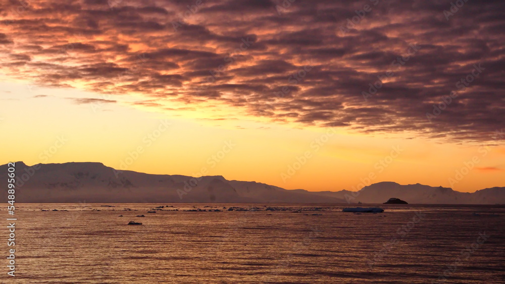 Pink clouds in an orange sky, with mountains and icebergs in silhouette, at Cierva Cove, Antarctica, at sunset