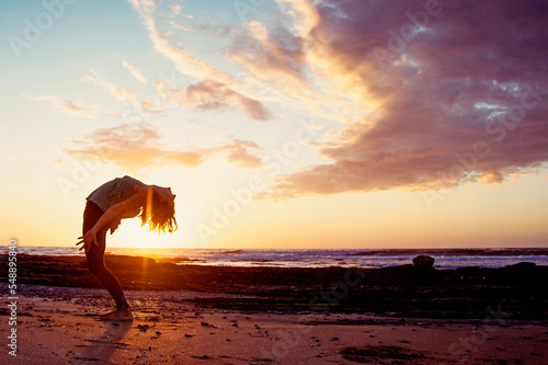 Joyful woman on a beach playing with a yoga pose in the sunset light. 