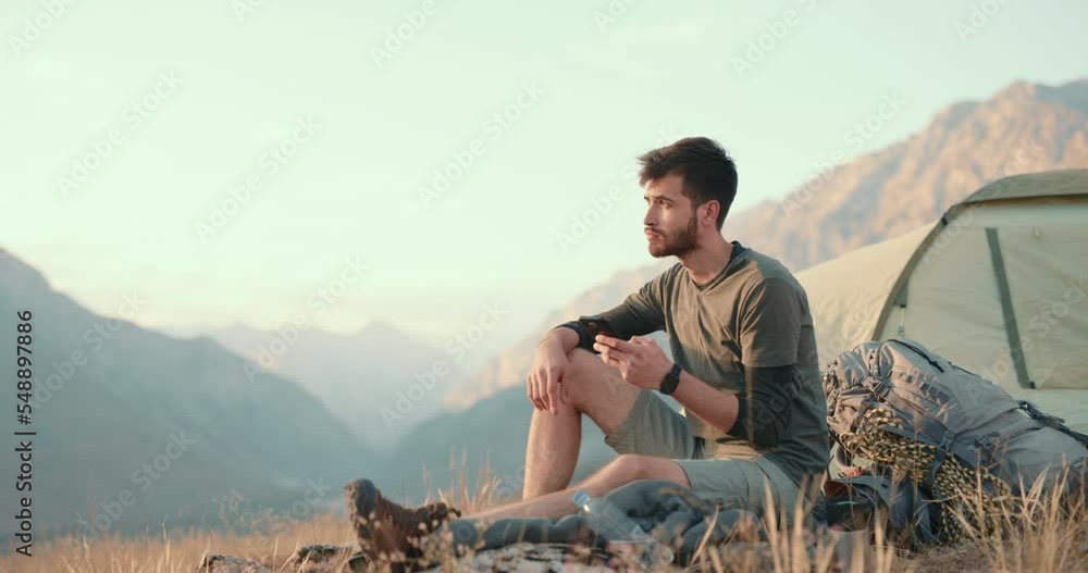 male tourist, hiking tourist uses his phone on a mountain top on a sunny day under the sunlight. Beautiful view of the mountain landscape and the sunset. Excellent cellular connection