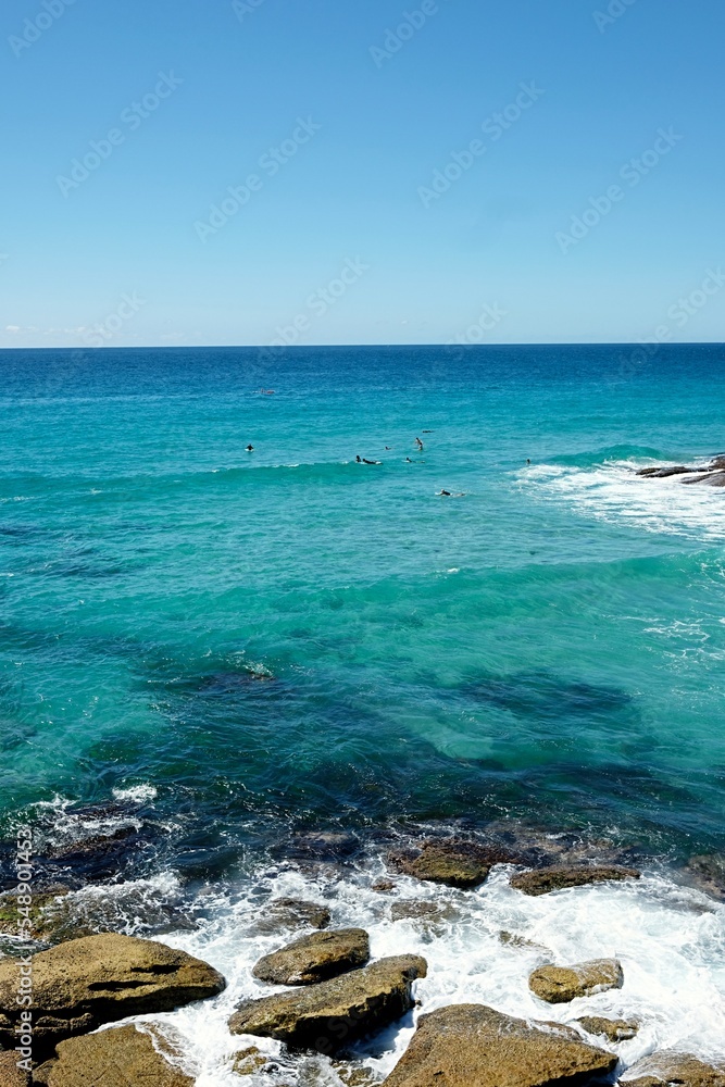 Cloudless blue skies and calm waters, waves crashing against the rocks along the Bondi to Bronte coastal walk — Tamarama, Sydney; New South Wales, Australia