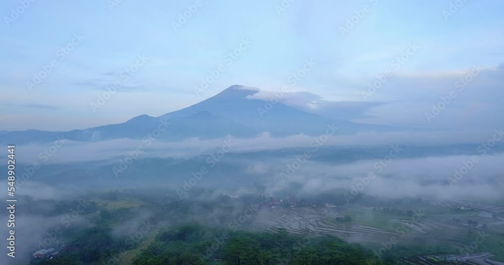 Aerial view over tropical countryside shrouded in a sea of mist with huge mountain on the background Aerial view over tropical countryside shrouded in a sea of mist with huge mountain on the background