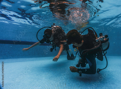 diving instructor teaches students to scuba dive in swimming pool. couple getting first experience with scuba diving under the guidance of experienced recreational diving instructor on vacation. photo