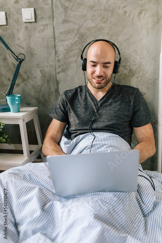 Man working from home, using laptop in bed